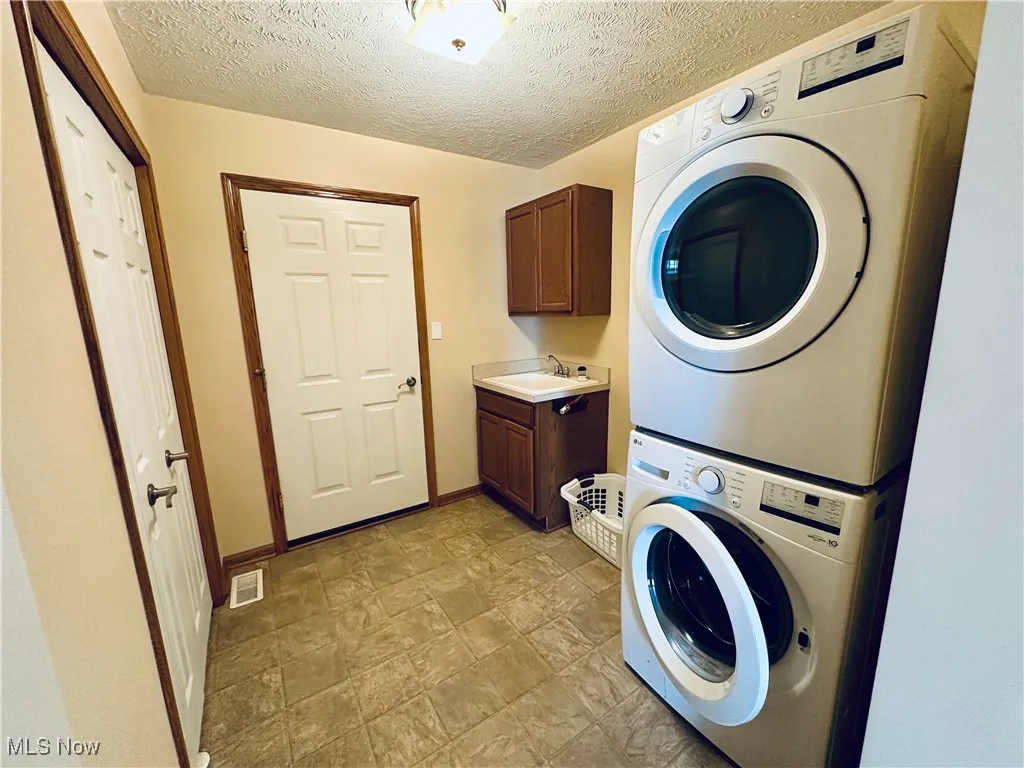 Washroom featuring stacked washer / dryer, a utility sink, and cabinet space.