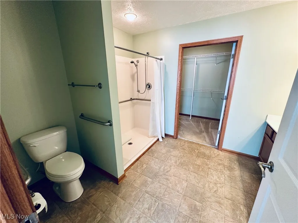 Full bathroom with a textured ceiling, vanity, a shower stall, and a spacious closet.