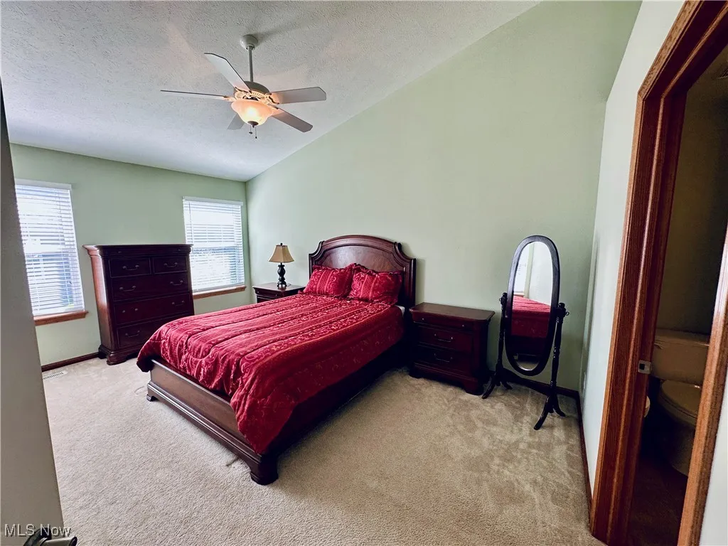 Bedroom featuring lofted ceiling, a textured ceiling, carpet floors, and ceiling fan.