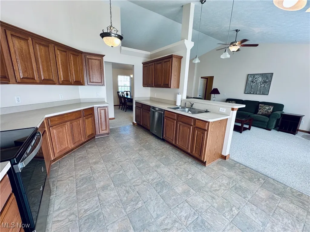 Kitchen with black / electric stove, open floor plan, lofted ceiling, light countertops, and light carpet.