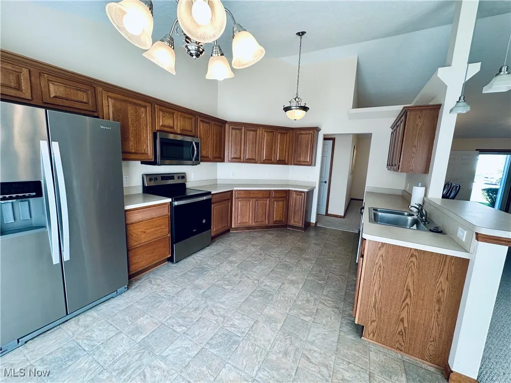 Kitchen with stainless steel appliances, brown cabinets, light countertops, pendant lighting, and high vaulted ceiling.
