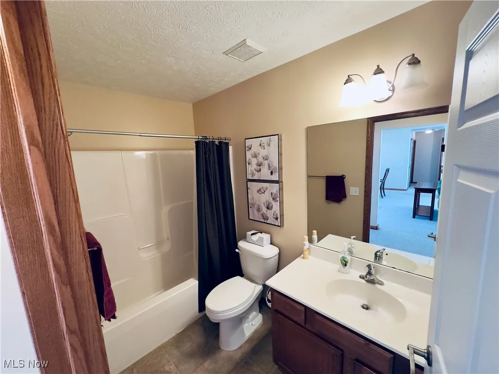 Full bathroom featuring a textured ceiling, vanity, shower / bathtub combination with curtain, and dark tile patterned floors