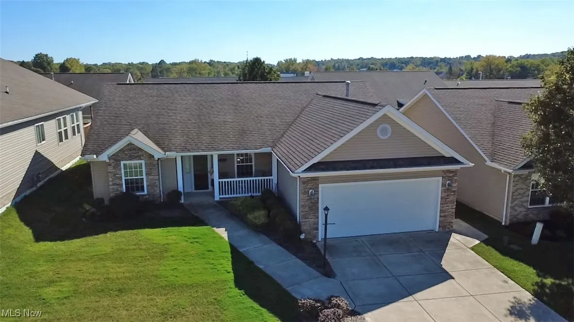 View of front facade with stone siding, a front yard, covered porch, driveway, and a garage.