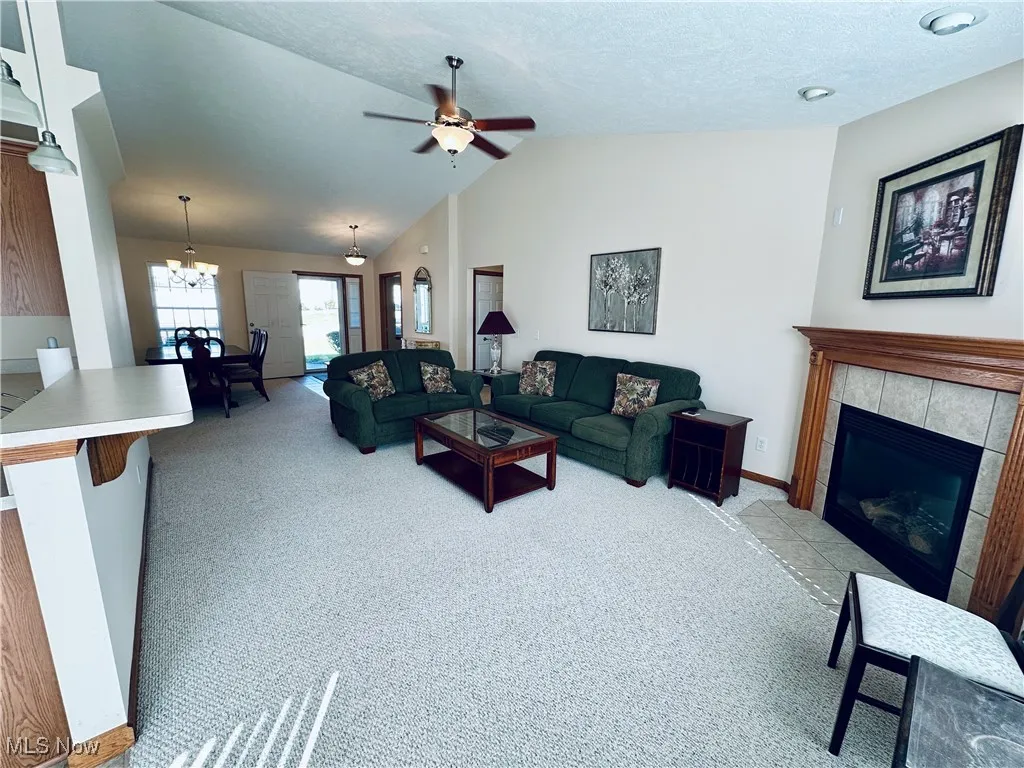 Living room with vaulted ceiling, a tile fireplace, light colored carpet, ceiling fan, and a textured ceiling.