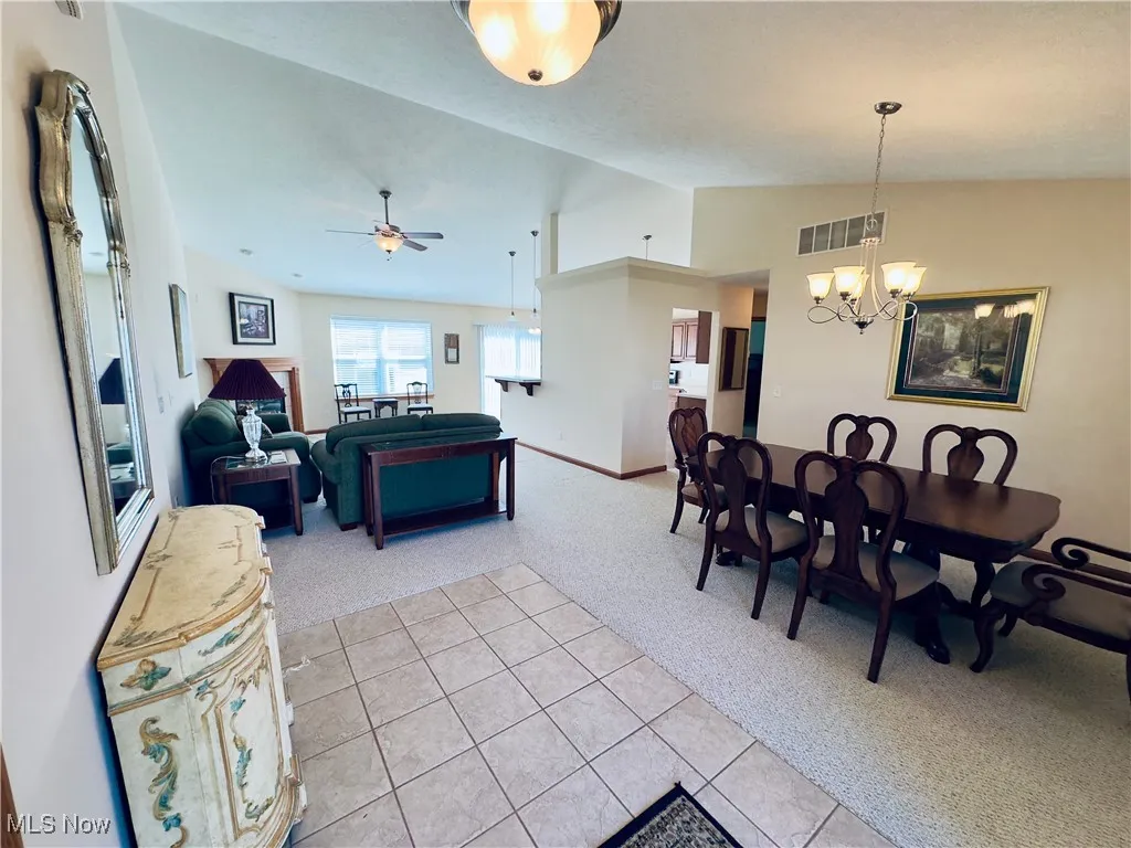 Dining area featuring light colored carpet, vaulted ceiling, a chandelier, light tile patterned flooring, and ceiling fan