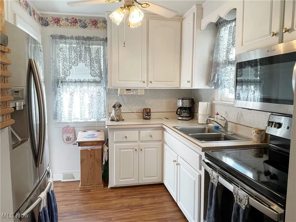 Kitchen with stainless steel appliances, light countertops, dark wood-style flooring, and white cabinetry