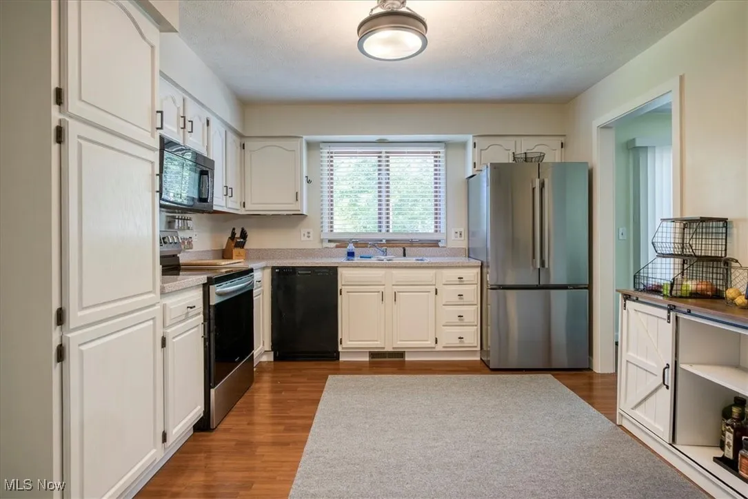 Kitchen featuring black appliances, dark wood-style flooring, white cabinets, and a textured ceiling