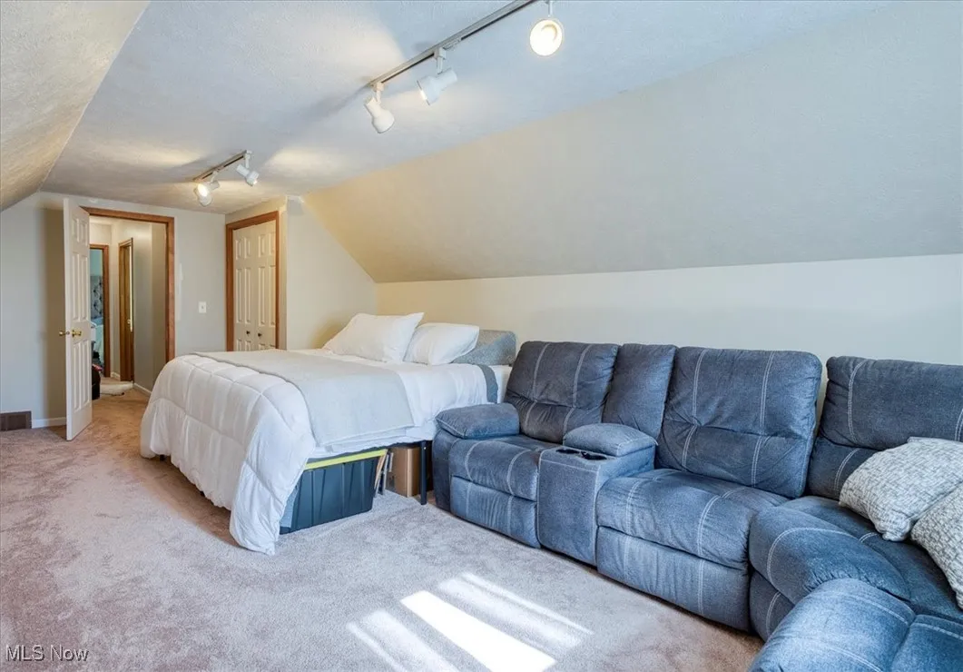 Carpeted bedroom with vaulted ceiling, track lighting, a closet, and a textured ceiling
