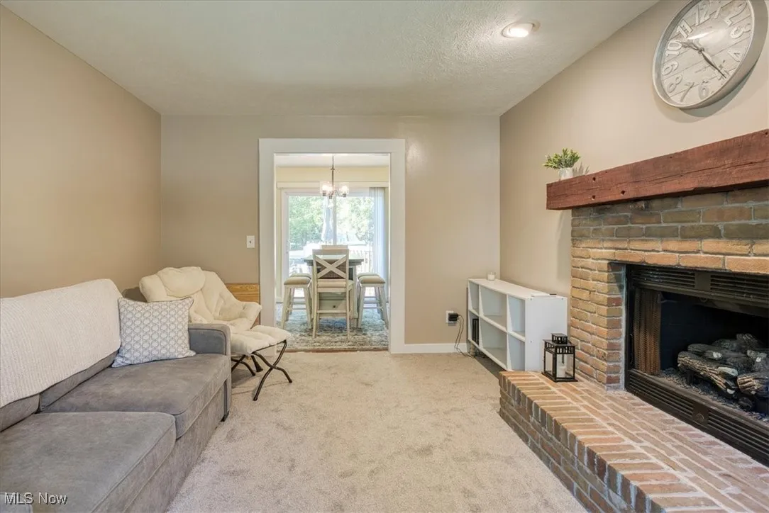 Living room with carpet, a brick fireplace, a textured ceiling, and a chandelier