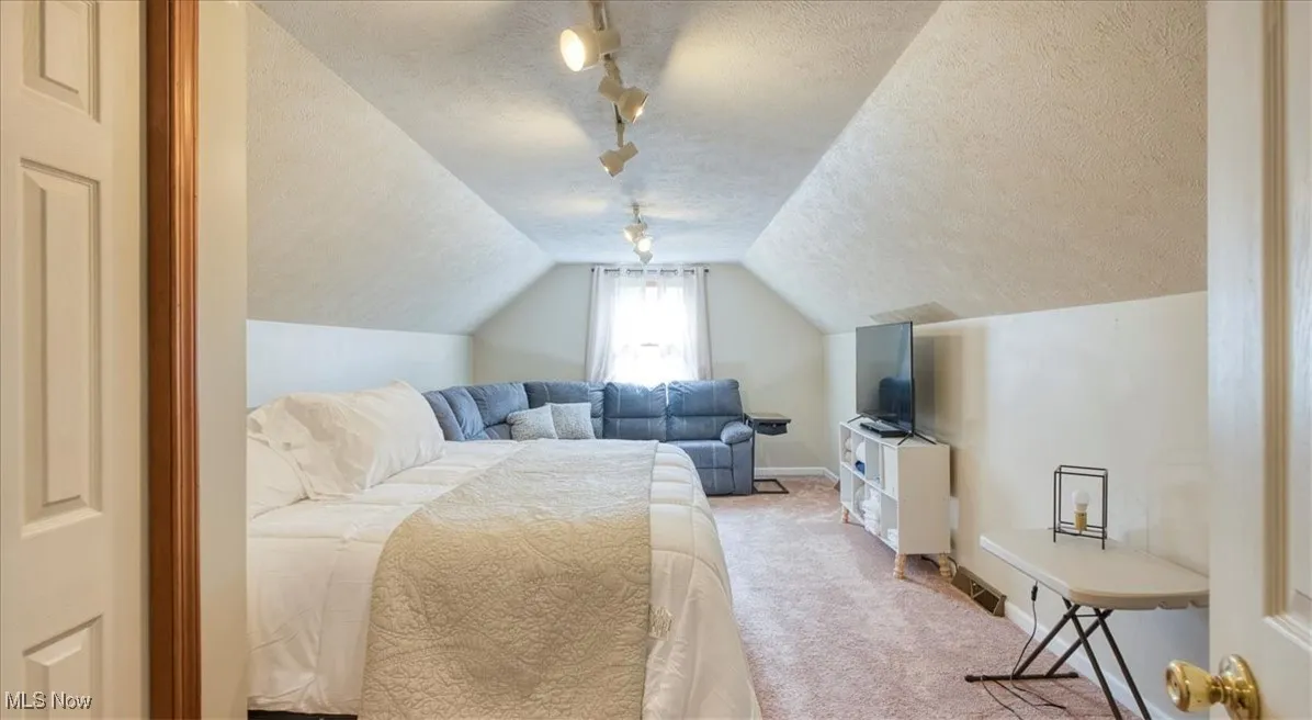 Bedroom with a textured ceiling, carpet flooring, lofted ceiling, and rail lighting