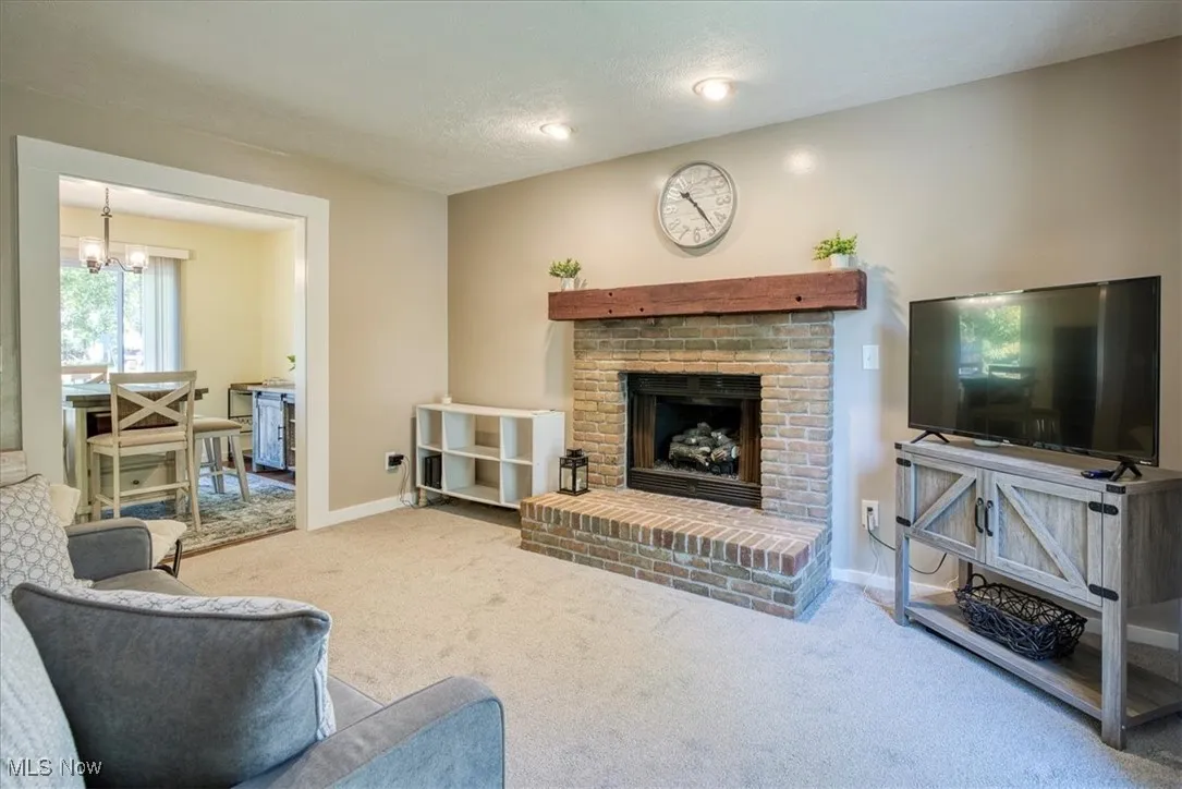 Living area with carpet floors, a brick fireplace, a chandelier, and a textured ceiling