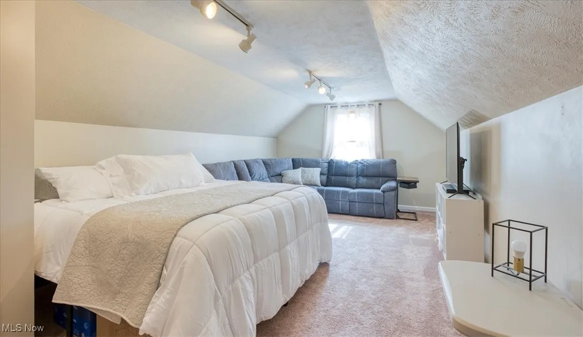 Carpeted bedroom featuring track lighting, vaulted ceiling, and a textured ceiling