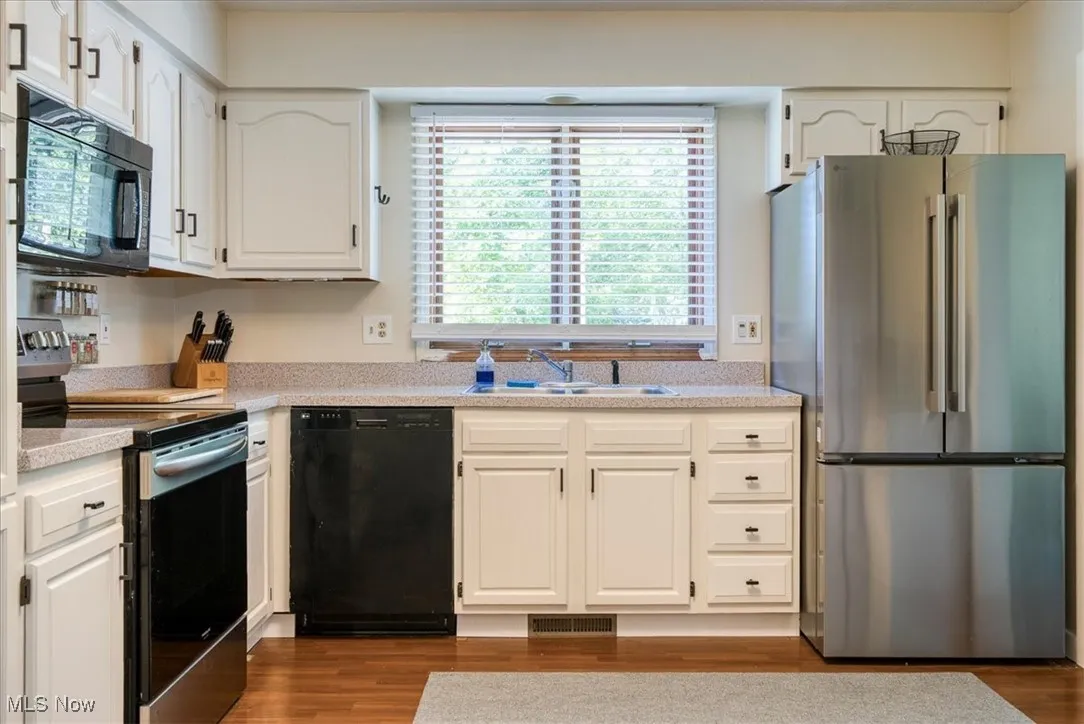 Kitchen with black appliances, dark wood-type flooring, and white cabinetry