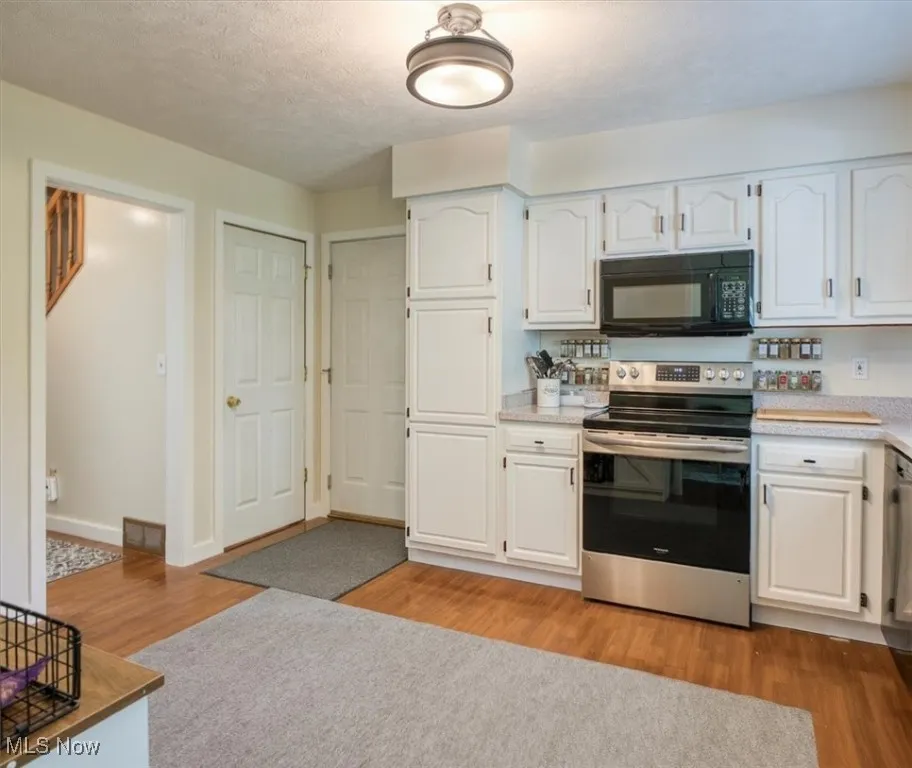 Kitchen featuring white cabinetry, appliances with stainless steel finishes, a textured ceiling, and light wood-type flooring