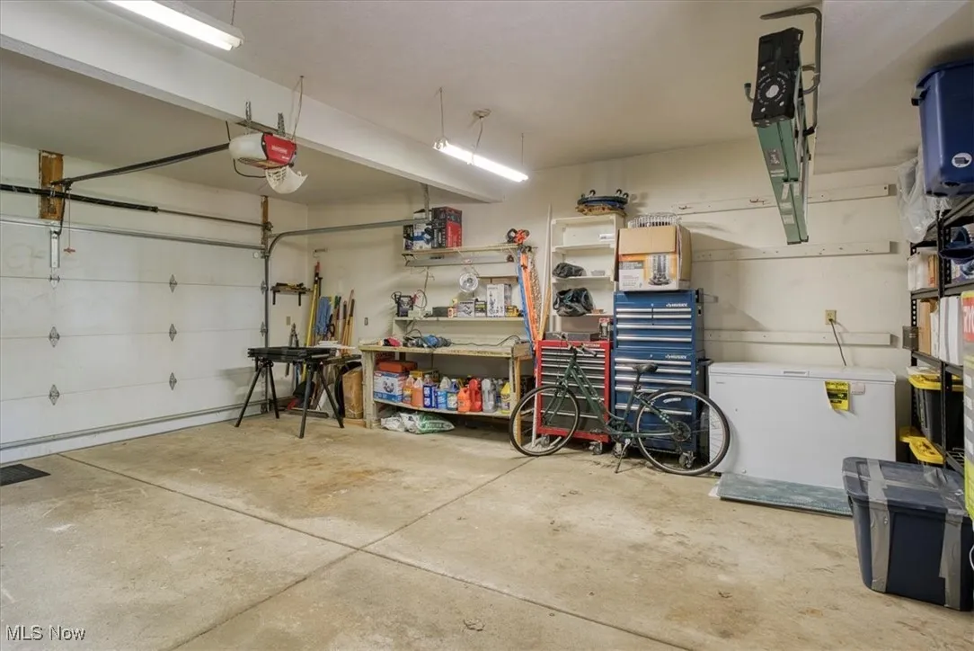 Garage featuring white refrigerator, a workshop area, and a garage door opener