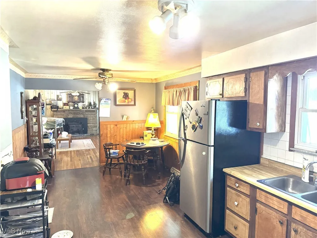 Kitchen with light countertops, wainscoting, dark wood-style floors, freestanding refrigerator, and a ceiling fan