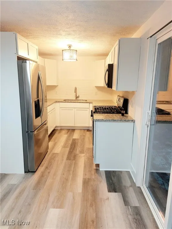 Kitchen featuring light stone counters, a textured ceiling, appliances with stainless steel finishes, white cabinetry, and light wood finished floors