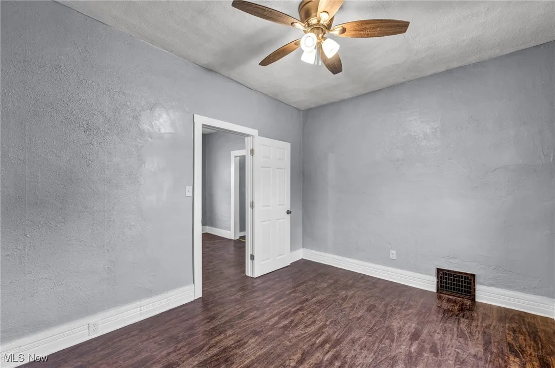 Empty room with a textured wall, dark wood finished floors, and ceiling fan