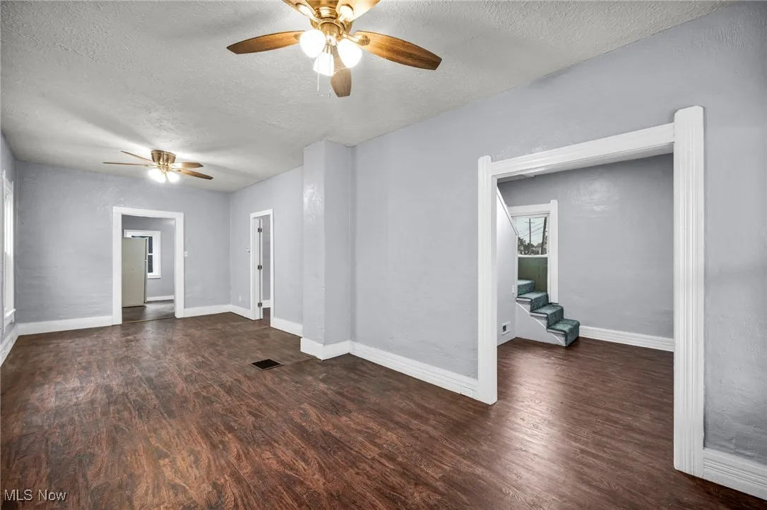 Empty room with a textured ceiling, dark wood-style floors, ceiling fan, and stairs