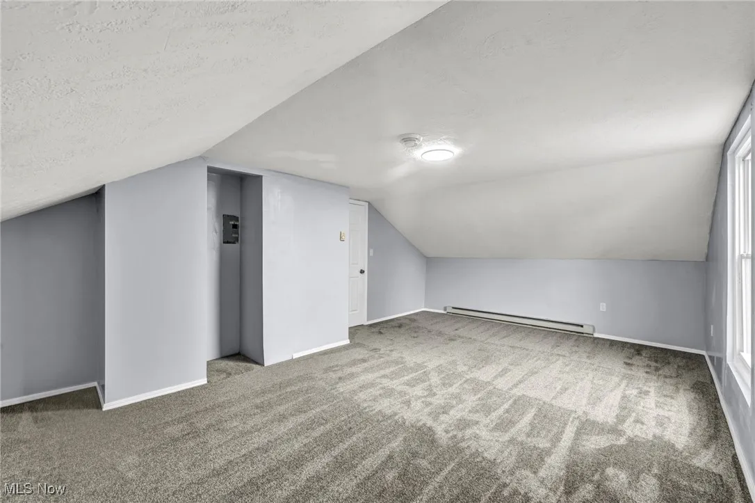 Bonus room featuring light carpet, a textured ceiling, vaulted ceiling, baseboard heating, and elevator