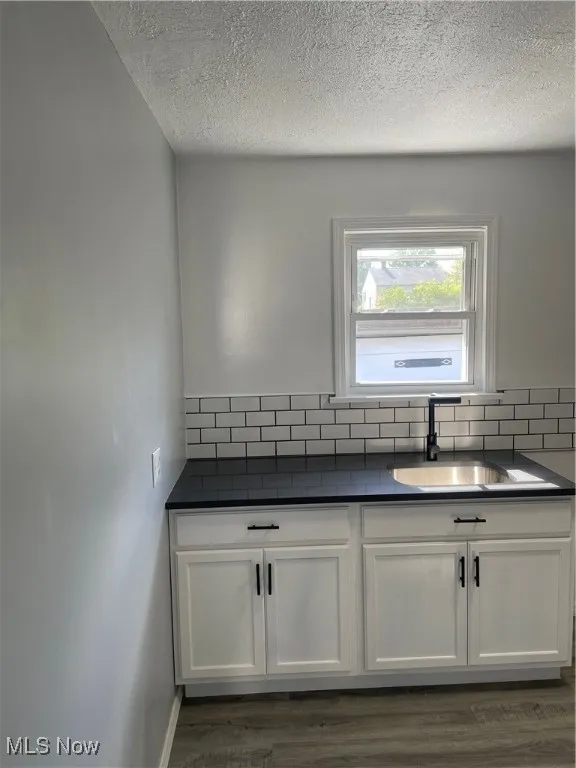 Kitchen with white cabinets, a textured ceiling, dark wood-type flooring, and backsplash