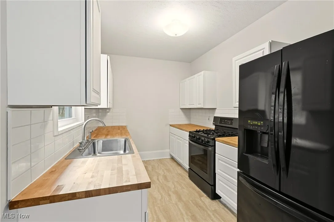 Kitchen featuring black appliances, white cabinets, tasteful backsplash, and butcher block counters