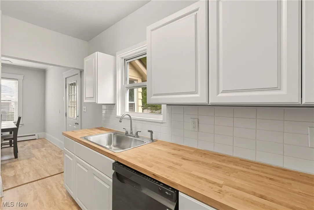 Kitchen with decorative backsplash, white cabinetry, and dishwasher