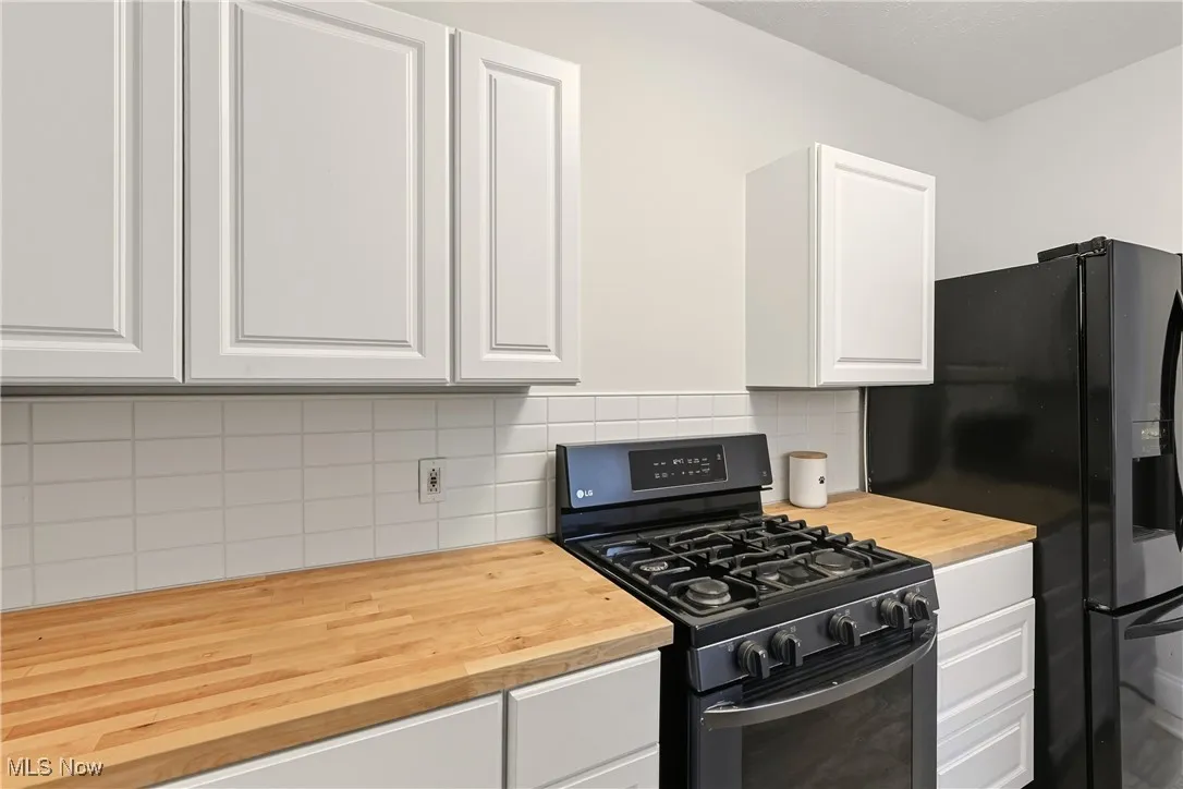 Kitchen with white cabinets, black appliances, and tasteful backsplash