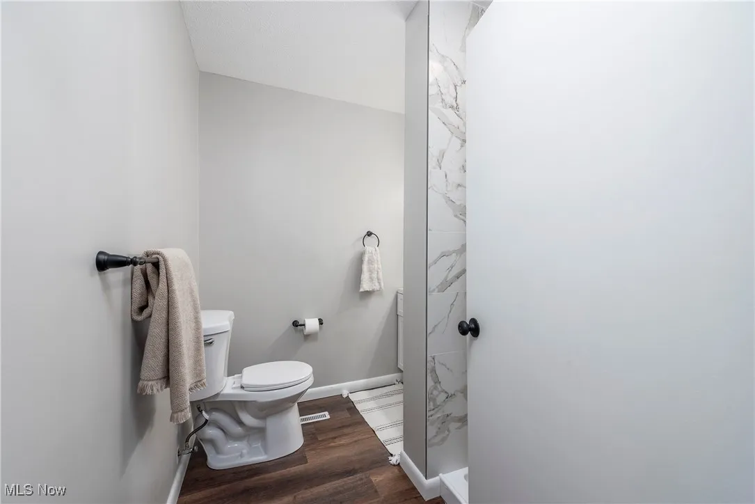 Full bath with a marble finish shower and dark wood-type flooring