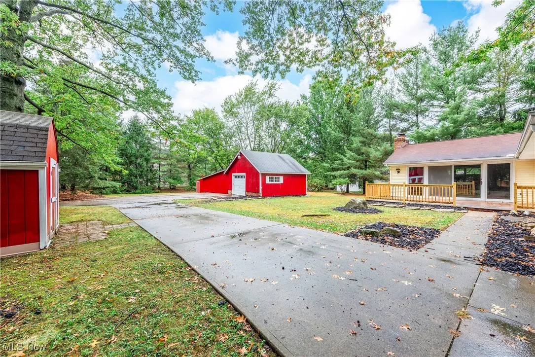 View of grassy yard featuring an outbuilding, a detached garage, covered porch, and view of scattered trees