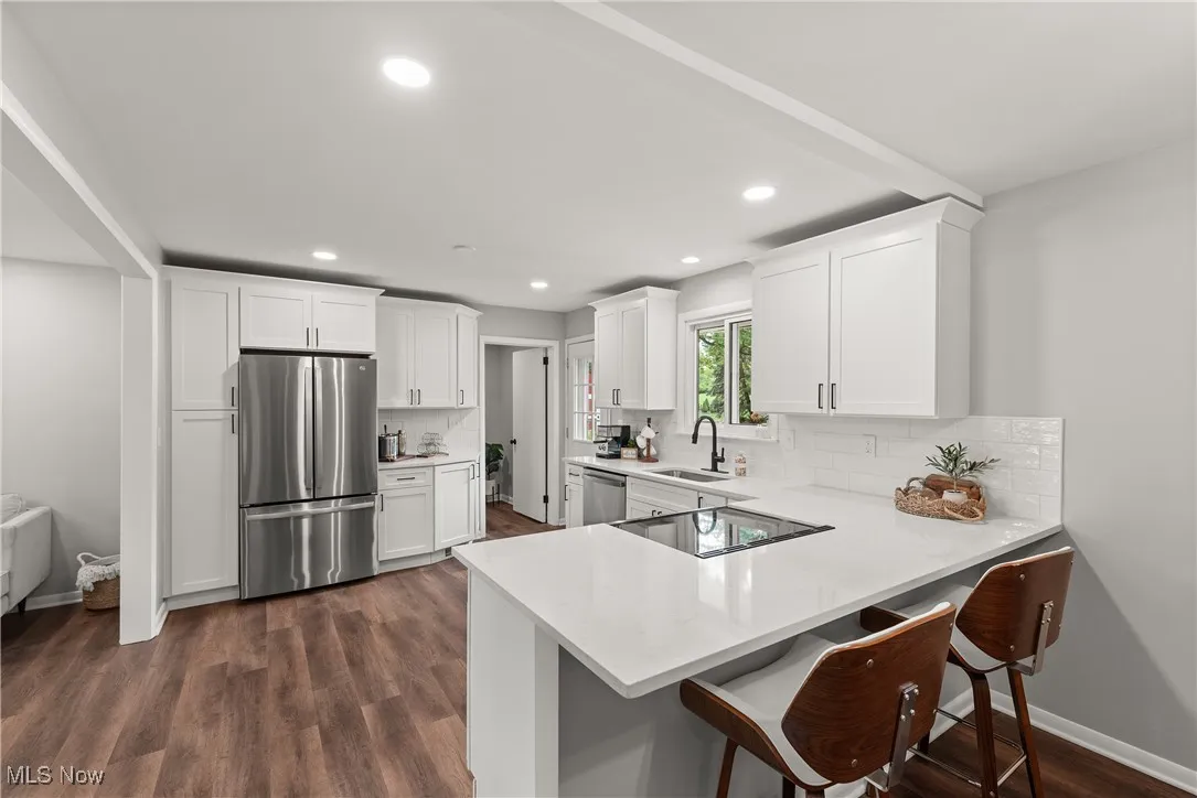 Kitchen featuring a kitchen breakfast bar, stainless steel appliances, white cabinets, tasteful backsplash, and dark wood-type flooring