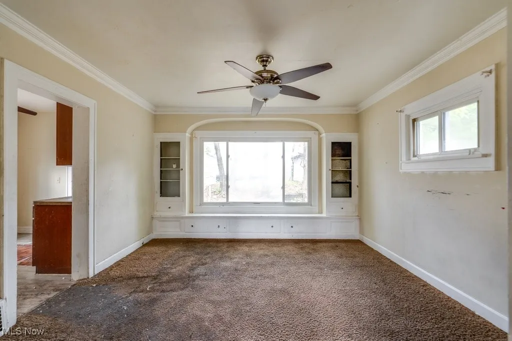 Empty room with ceiling fan, healthy amount of natural light, crown molding, and carpet flooring