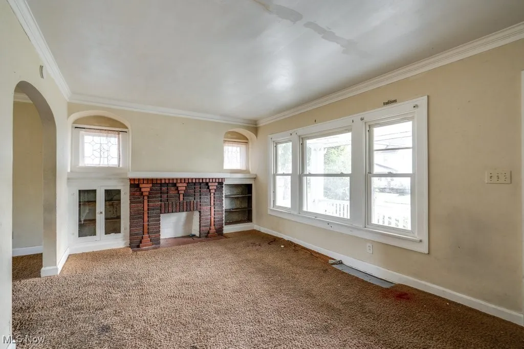 Unfurnished living room with carpet, crown molding, plenty of natural light, a fireplace, and arched walkways