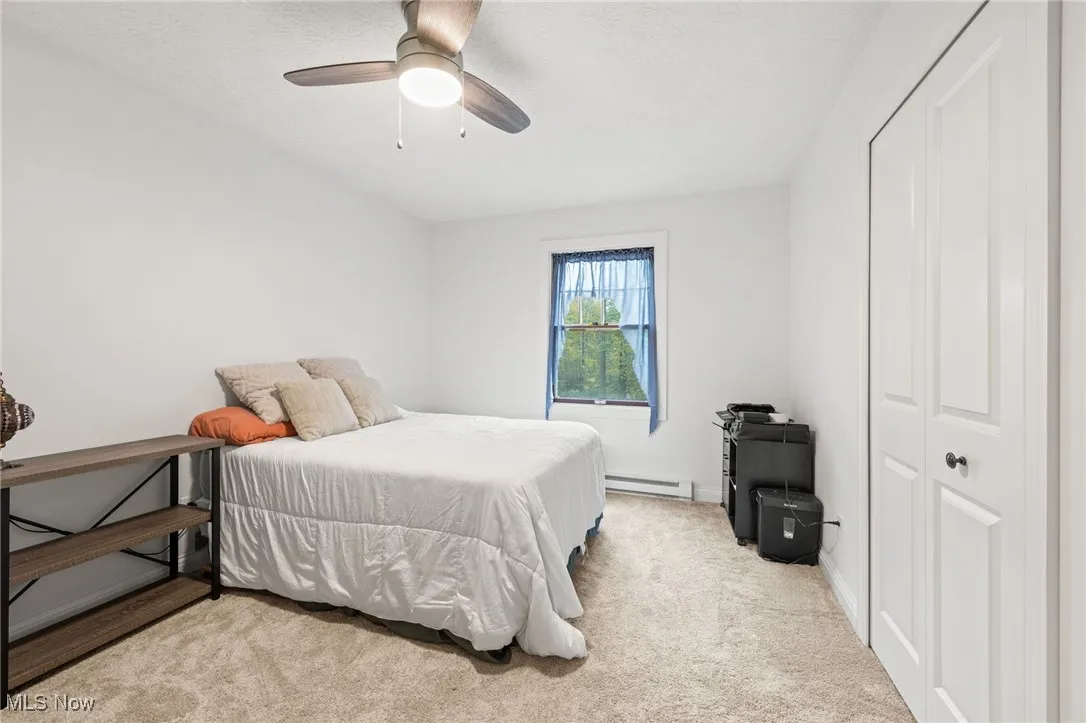 Bedroom featuring light carpet, a ceiling fan, a closet, a baseboard heating unit, and a textured ceiling