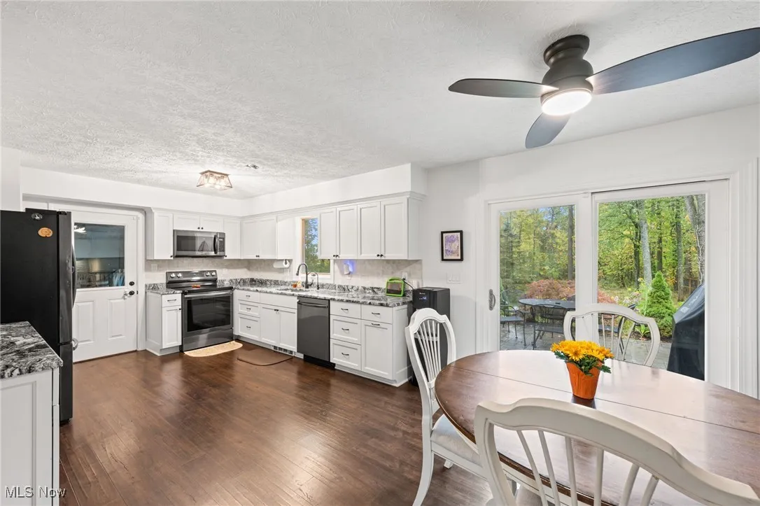 Kitchen featuring stainless steel appliances, white cabinetry, a textured ceiling, dark wood finished floors, and plenty of natural light