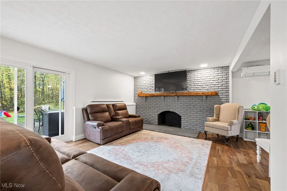 Living area featuring wood finished floors, a textured ceiling, a fireplace, a wall mounted AC, and recessed lighting
