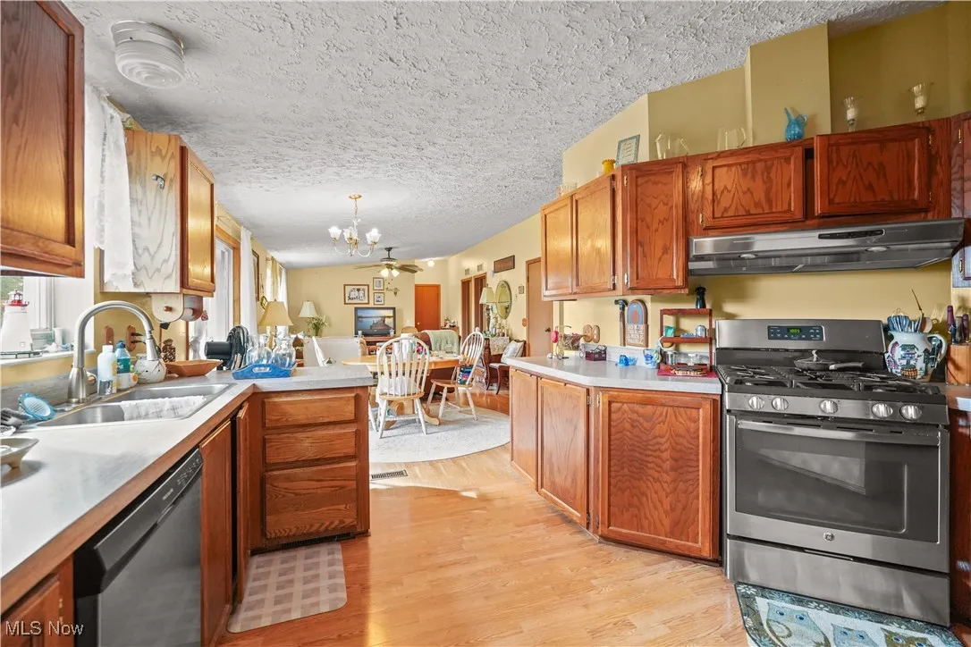Kitchen with stainless steel range with gas stovetop, light wood-type flooring, dishwasher, brown cabinetry, and under cabinet range hood