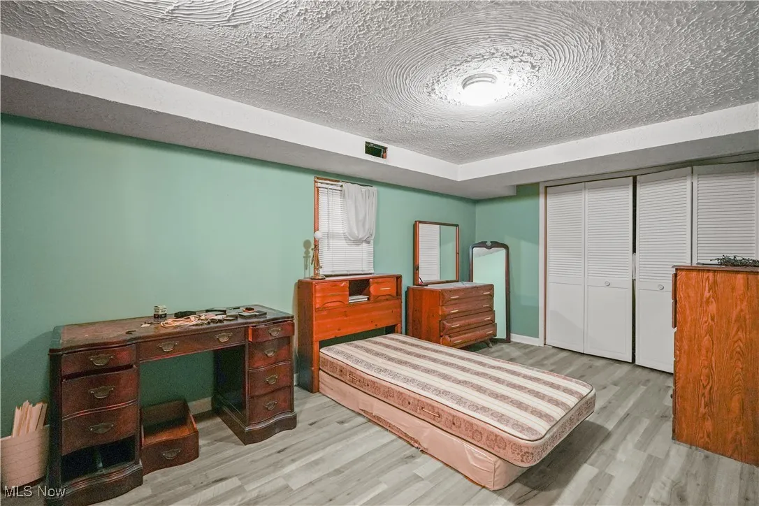 Bedroom with a textured ceiling, light wood-style floors, and a closet