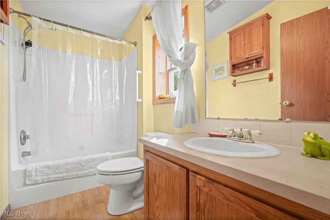 Bathroom featuring shower / bath combo, light wood-style floors, vanity, and decorative backsplash