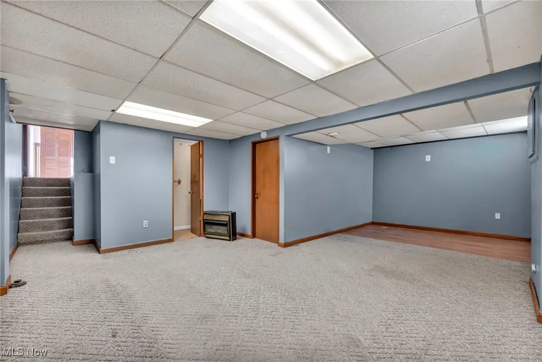 Below grade area with carpet flooring, a paneled ceiling, and stairway