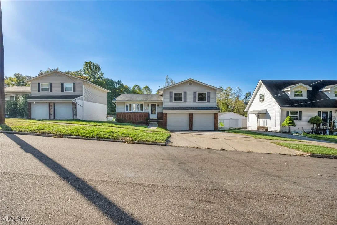 Tri-level home with driveway, an attached garage, brick siding, and a front lawn