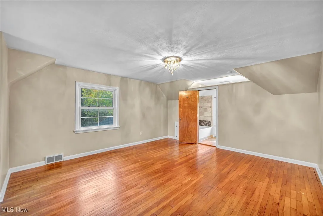 Additional living space with light wood-style flooring, lofted ceiling, a chandelier, and a textured ceiling