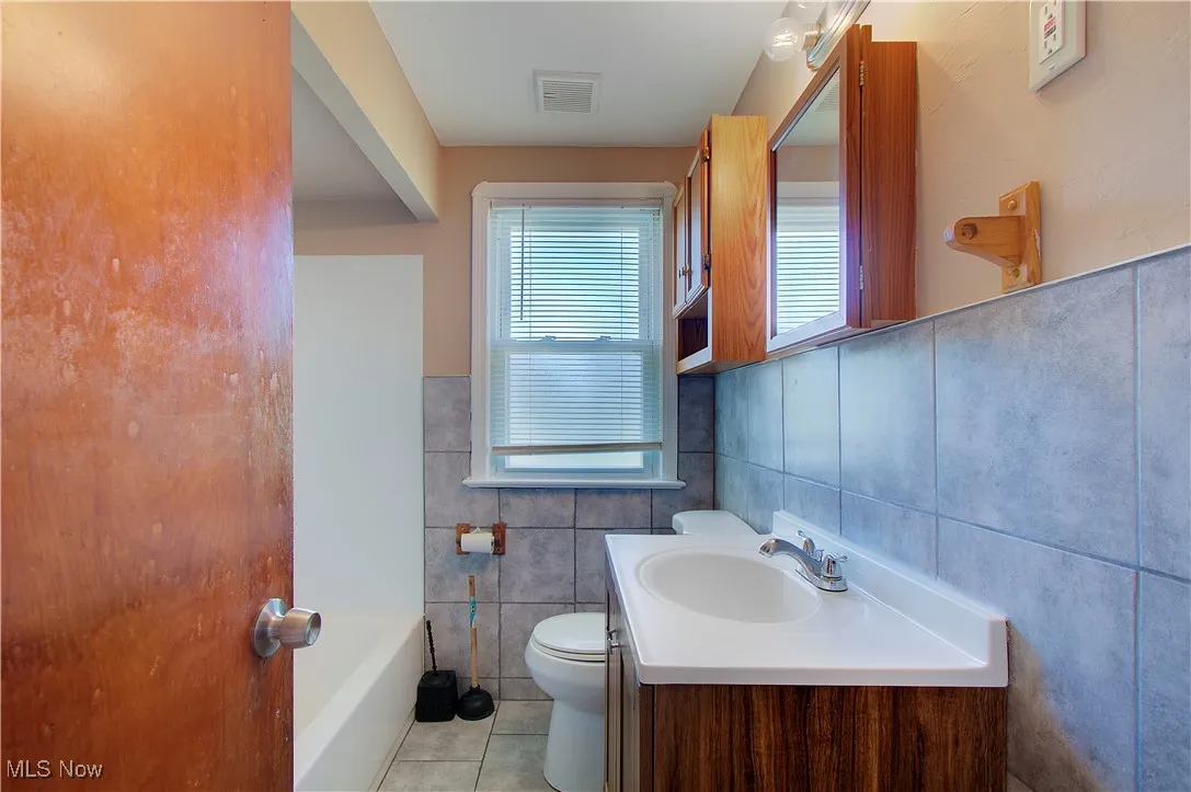 Bathroom with tile walls, vanity, light tile patterned floors, and a bathtub