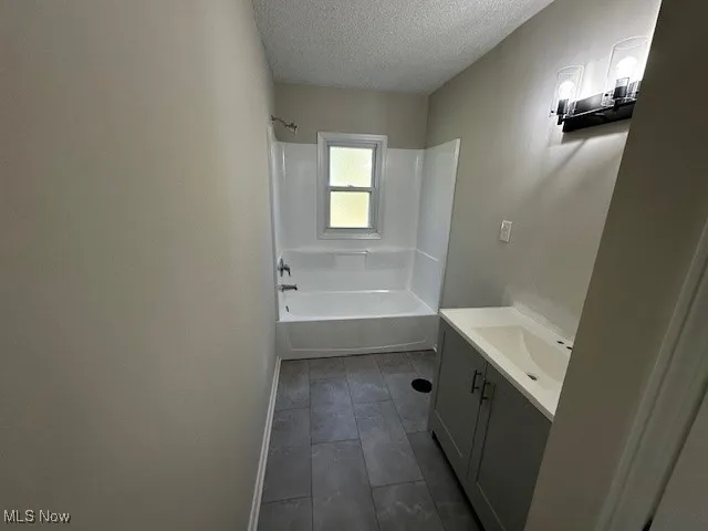 Full bath with a textured ceiling, bathing tub / shower combination, and vanity