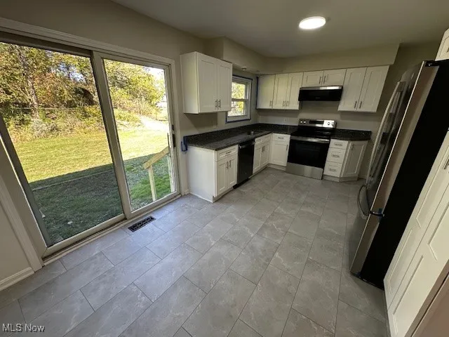 Kitchen featuring stainless steel appliances, white cabinets, ventilation hood, and dark stone countertops