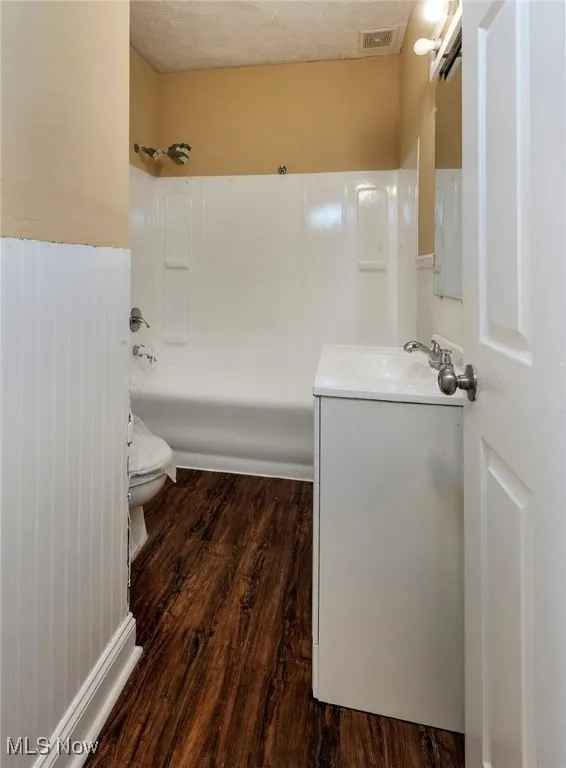 Bathroom with dark wood finished floors, vanity, shower / washtub combination, and a textured ceiling