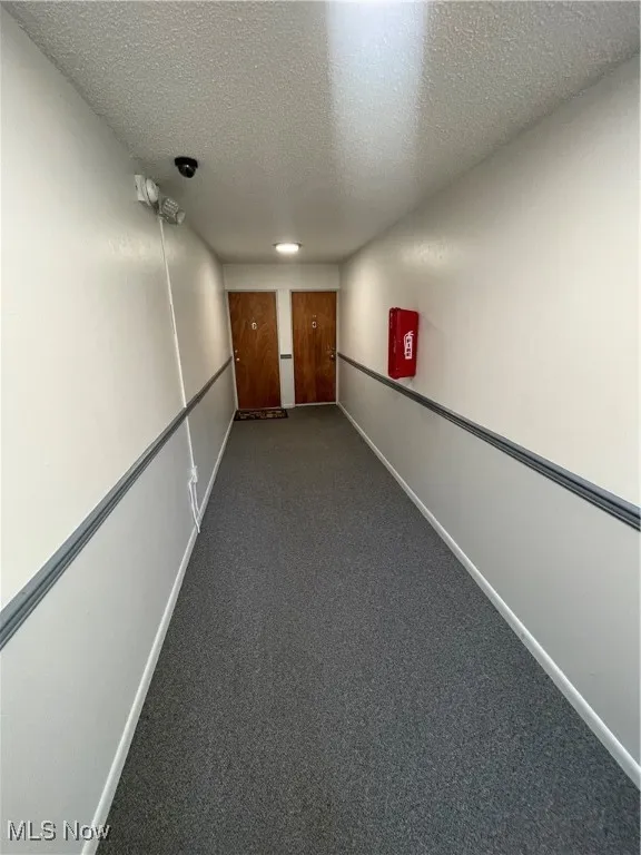 Corridor featuring a textured ceiling and dark colored carpet