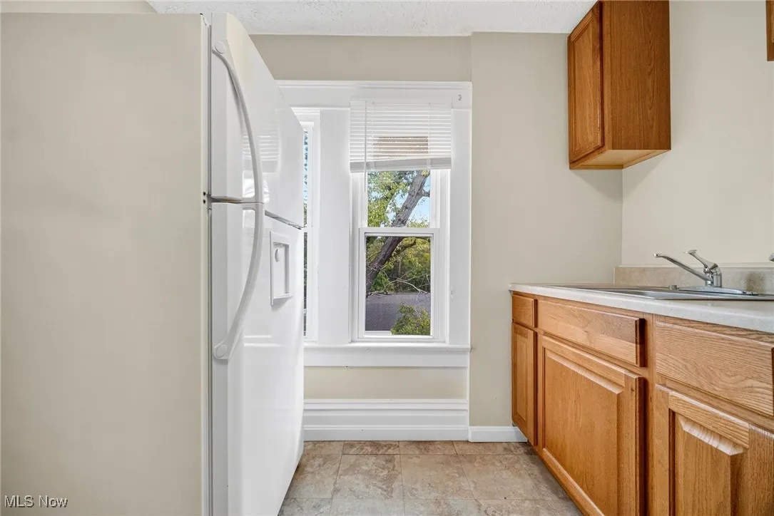 Kitchen with freestanding refrigerator, brown cabinets, light countertops, and a textured ceiling