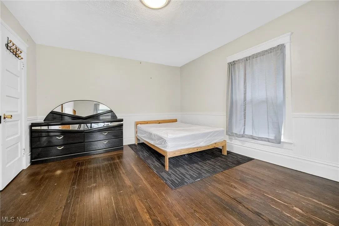 Bedroom with dark wood-type flooring, a textured ceiling, and a wainscoted wall