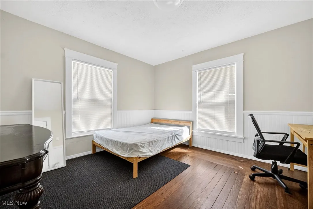 Bedroom with dark wood-style floors, a wainscoted wall, a textured ceiling, multiple windows, and an office area